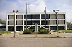 A three-story government building, home to the Louisiana Office of the State Public Defender, features two flagpoles and a central staircase leading to its entrance.