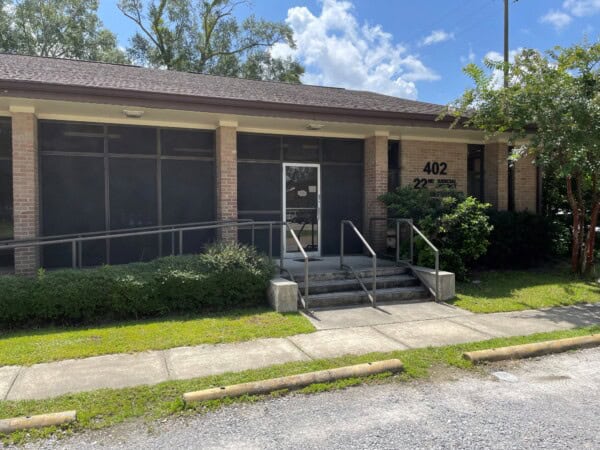 A single-story brick building with a glass entrance, labeled "402," houses the Louisiana Public Defender's Office. It is surrounded by greenery under a partly cloudy sky, adding an air of tranquility to its important mission.