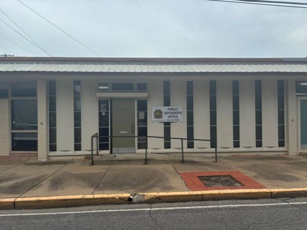 The glass entrance door of the District 9 Louisiana Office of the State Public Defender in Alexandria, LA, warmly invites visitors, flanked by a sign that stands tall against its vertical windows.