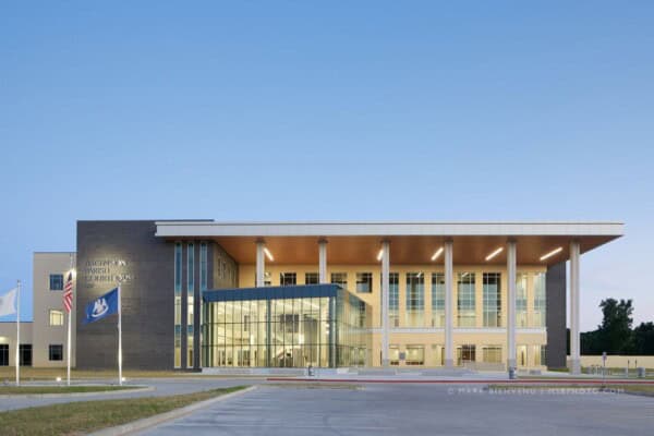 A modern courthouse building with large glass windows, columns, and a flat roof stands prominently. Two flags flank the entrance, symbolizing justice and roles such as those of the Louisiana Office of the State Public Defender.