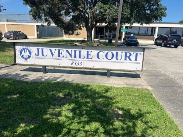 A sign reading "Juvenile Court 8333" stands in front of the building, framed by a tree and parked cars, while nearby the Louisiana Public Defender's Office works tirelessly to represent those in need.