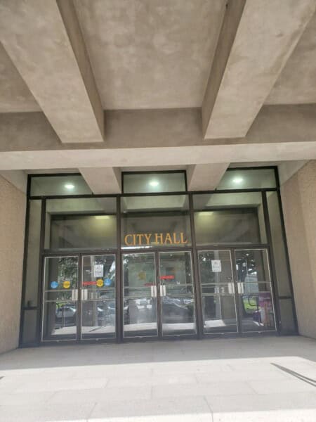The entrance of a building boasts "City Hall" signage above its glass doors, with overhead lights illuminating the pavement—a nearby branch of the Louisiana Office of the State Public Defender (LAOSPD).